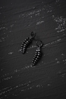 A pair of bold statement earrings with clean lines showcased on a matte black pedestal.
