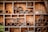 Wooden structure contains multiple hexagonal compartments, each filled with various natural materials like bamboo sticks and twigs, suggesting a habitat or nesting area for insects. The background is a rustic wooden surface, adding to the natural and earthy feel.