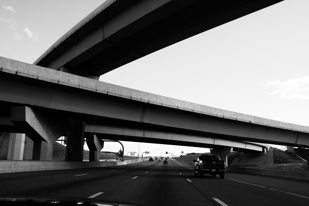 a black and white photo of a truck driving under a bridge