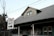 A residential house with a pitched roof and a smaller upper window. There is a 'One Way' street sign in the foreground pointing to the right. Bare trees and utility wires stretch across the sky, while the house features a porch with white columns and green siding.