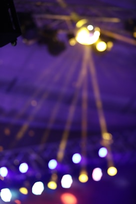 Bright, colorful stage lights create rays and lens flares against a blurred background, conveying a lively and dynamic atmosphere.