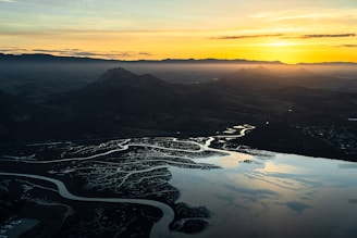 A breathtaking aerial shot of a winding mountain river at sunset with golden light reflecting on the water.