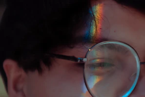 Side profile of a person wearing šviesprisma frames, with the lens catching light and displaying rainbow hues.