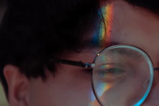 Side profile of a person wearing šviesprisma frames, with the lens catching light and displaying rainbow hues.