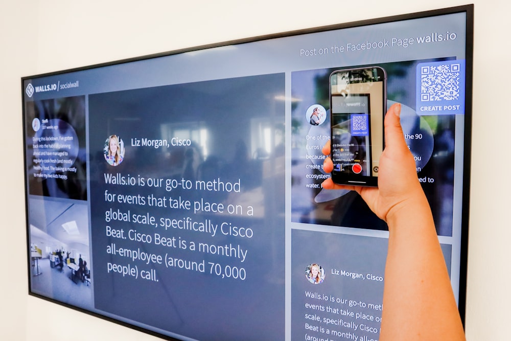 a person holding a cell phone in front of a large screen