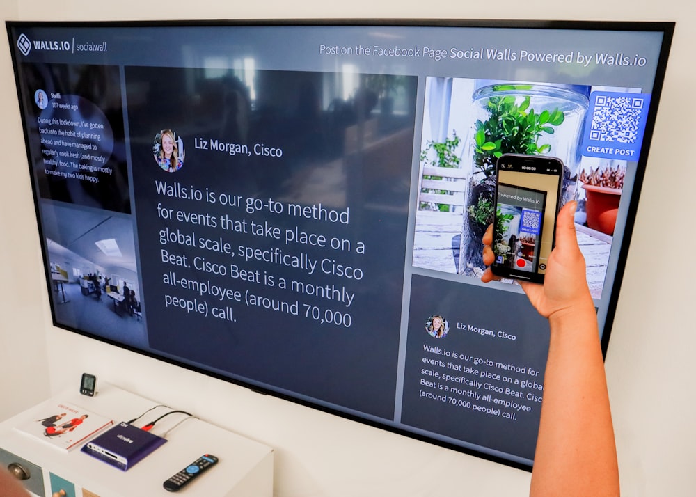 a person holding a cell phone in front of a large screen