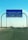A blue road sign indicating directions to Al Khafji Port in the Kingdom of Saudi Arabia. It provides separate lanes for passengers and cargo trucks. Cars are seen traveling on the highway beneath a clear blue sky.