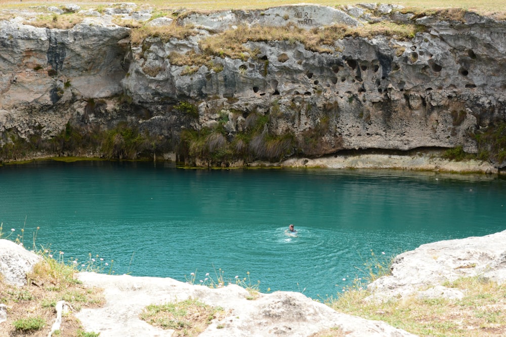 a man swimming in a pool of water near a cliff