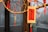 A decorative wooden plaque with Chinese calligraphy hangs on a branch adorned with vibrant red tassels and small ornaments. The background appears to be a blurred interior space.