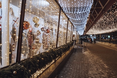 A commercial storefront featuring elegant white lights outlining windows and rooflines with festive music playing.