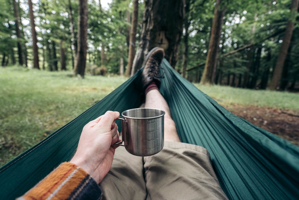 a person laying in a hammock with a cup of coffee