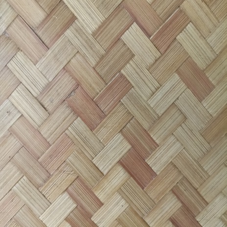 A detailed pattern of interwoven strips creating a textured, basket-like surface. The natural fibers have varying shades of beige and brown, highlighting the woven craftsmanship.