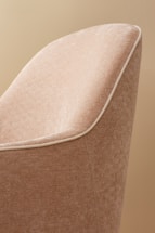 A close-up view of a fabric-covered chair with a textured pattern in shades of beige. The chair features white piping along the edges, creating a clean and elegant outline.