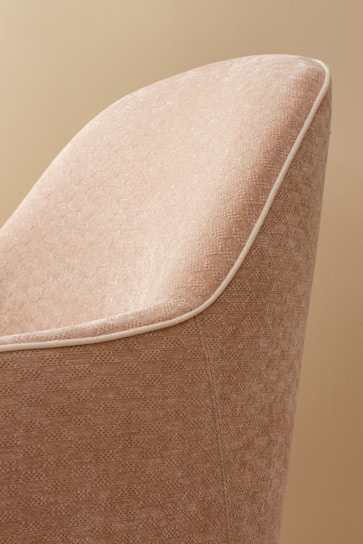 A close-up view of a fabric-covered chair with a textured pattern in shades of beige. The chair features white piping along the edges, creating a clean and elegant outline.