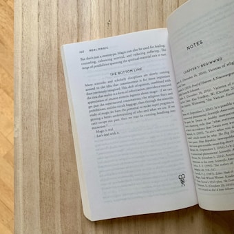 A wooden surface with an open book displaying two pages. The left page contains text discussing the concept of real magic and its potential uses in healing and consciousness studies. The page number is 222. The right page, titled 'Notes,' includes references and citations for various sources.