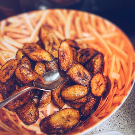 Close-up of a rich, golden peanut sauce drizzled over steaming plantains on a rustic wooden plate.