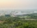 A sprawling campus with multiple buildings surrounded by lush greenery. The architecture features a mix of modern and traditional designs, with a prominent central building flanked by others. The horizon shows a hazy skyline with distant hills under a serene sky.