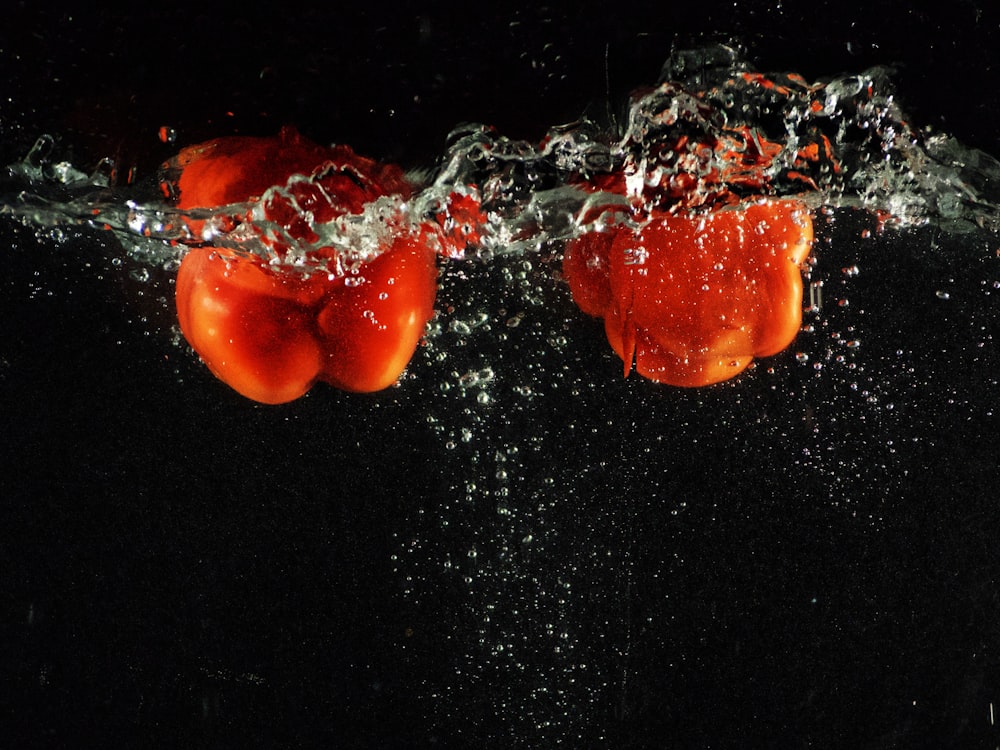 a group of tomatoes floating in water on a black background