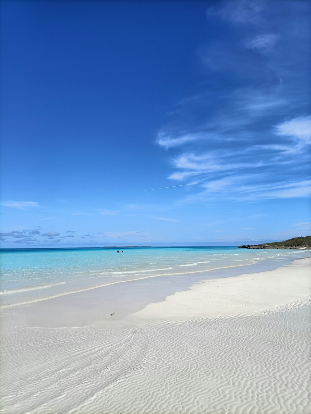 une plage de sable avec une eau bleue claire et un bateau au loin