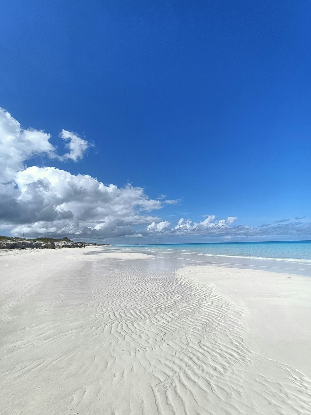 uma praia de areia com um céu azul e nuvens brancas