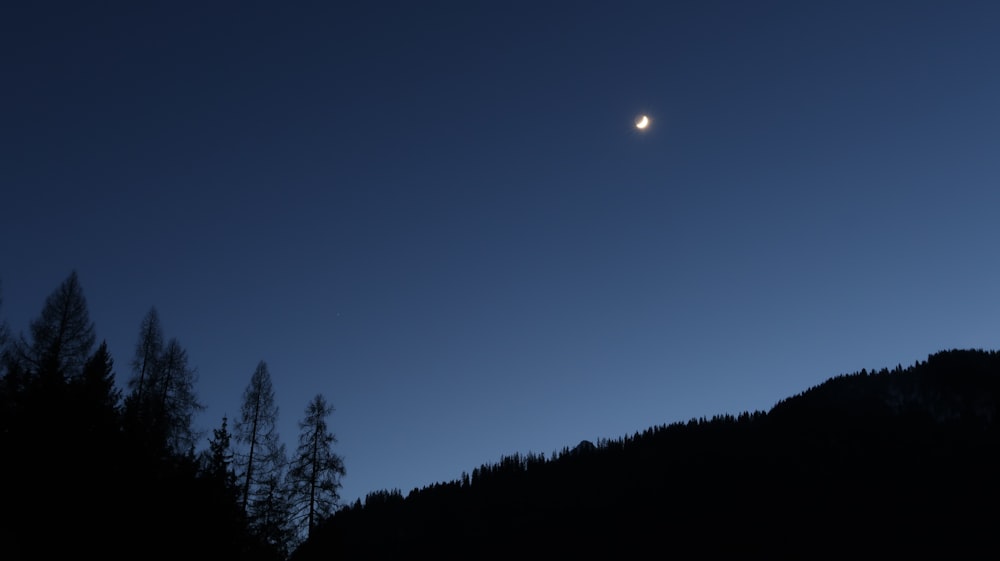 a full moon is seen in the sky above a mountain