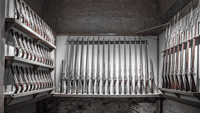 A display of new and used firearms neatly arranged on dark wooden racks under soft lighting.