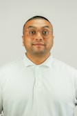 A man with short hair and glasses is wearing a light-colored polo shirt against a plain background.