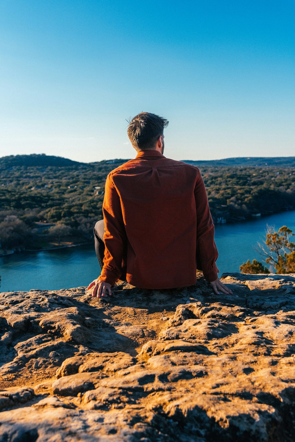 um homem sentado em cima de uma rocha ao lado de um lago