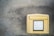 A yellow mailbox is mounted on a weathered concrete wall. The mailbox features a label with collection times and other information written in German.