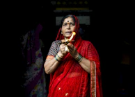 A little girl in a soft pink sharara set holding a diya, her face glowing with excitement during a festival evening.