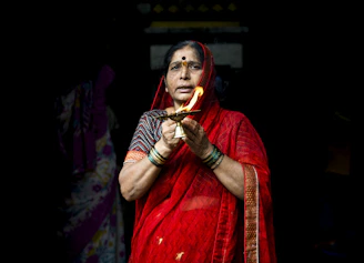 A little girl in a soft pink sharara set holding a diya, her face glowing with excitement during a festival evening.