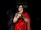A joyful woman in traditional attire sitting peacefully with a glowing diya in the background.