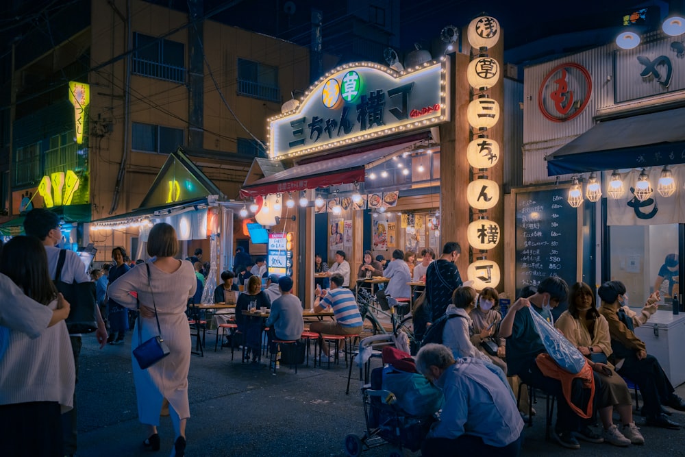 a group of people sitting outside of a restaurant at night