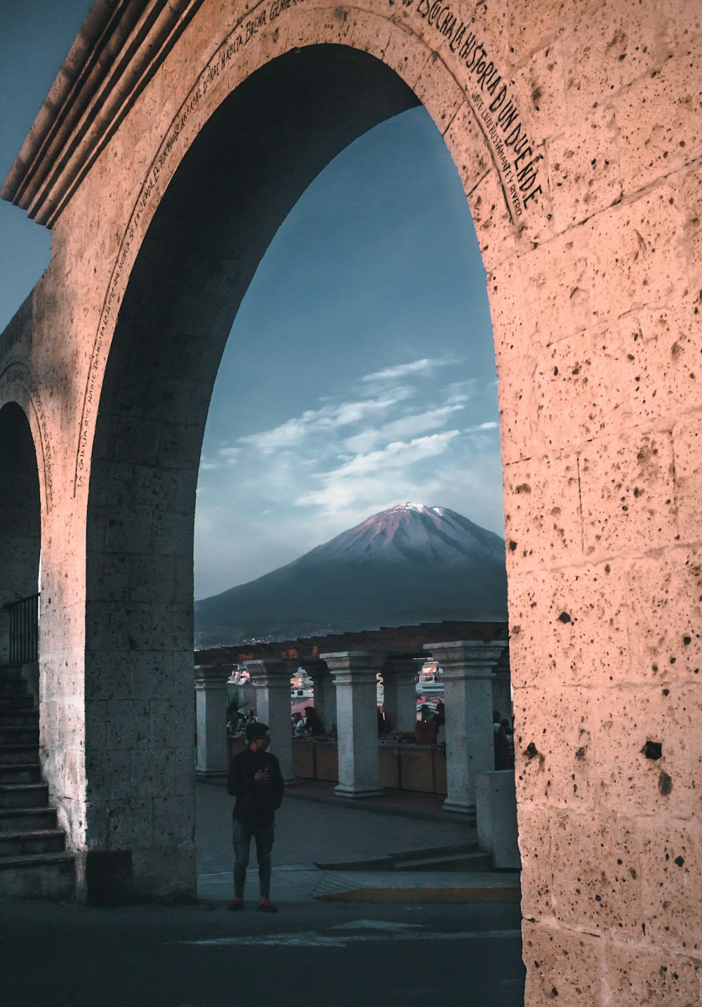 a person standing under an arch with a mountain in the background