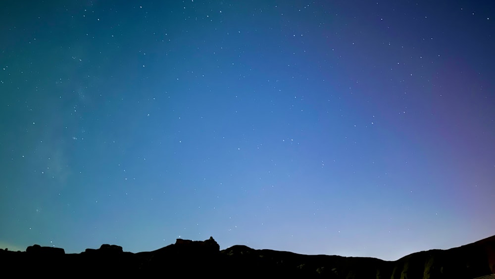 the night sky with stars above a mountain range