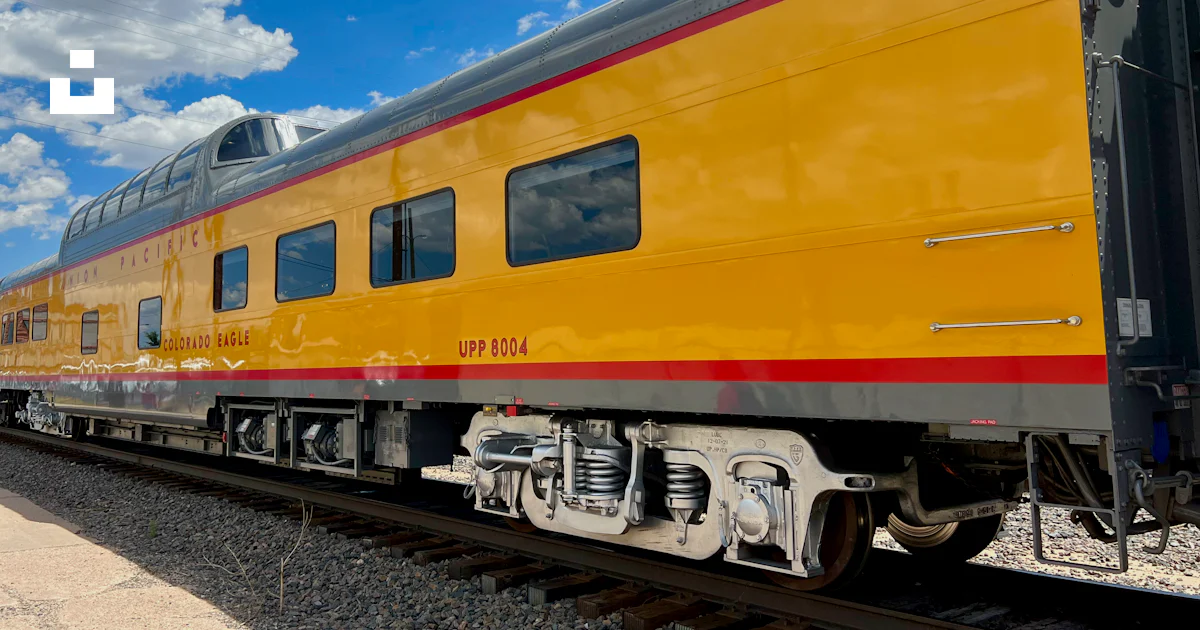 A yellow train traveling down train tracks under a blue sky photo ...