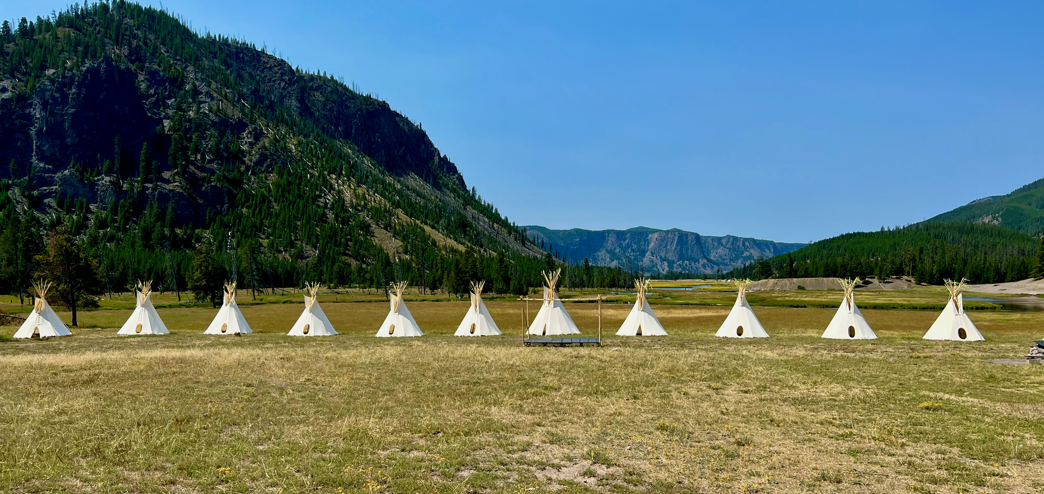 a group of teepees in a field with mountains in the background