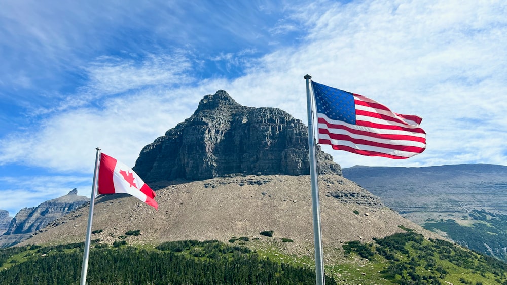 two american and canadian flags flying in front of a mountain