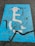 A weathered blue parking space marking on asphalt depicting a person in a wheelchair with a graduation cap and holding a diploma. The paint is cracked and faded, with a prominent black crack running across it.