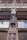 An intricately carved wooden facade features a statue of a person in historical attire. The architecture includes detailed window frames and decorative elements, creating a classic and artistic appearance. The craftsmanship is ornate, reflecting a style from a bygone era.