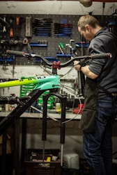 A craftsman assembling a retro-style bicycle with modern mechanical parts in a warm, off-white lit studio.