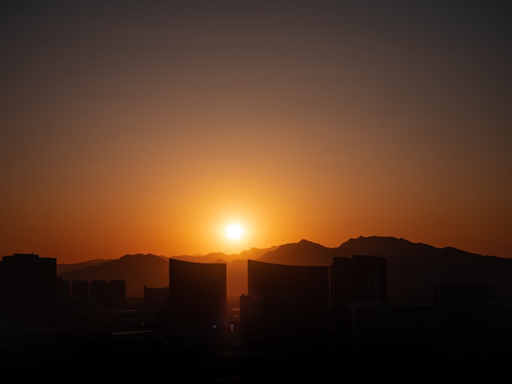 the sun is setting over a city with mountains in the background