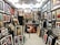 A gallery space filled with numerous framed artworks covering the walls and floor. The artworks range from abstract pieces to portraits and calligraphy, displayed in various sizes and frames. The room is well-lit with multiple ceiling lights, and there are some empty frames leaning against the walls.