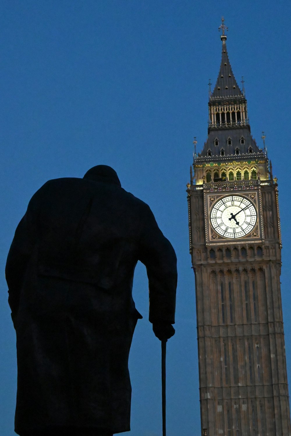 uma estátua de um homem com uma bengala em frente a uma torre do relógio