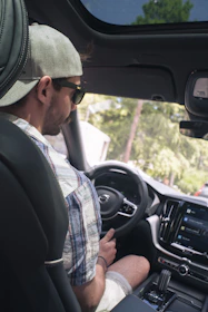A happy passenger using a smartphone app inside a modern car in a sunny city street.