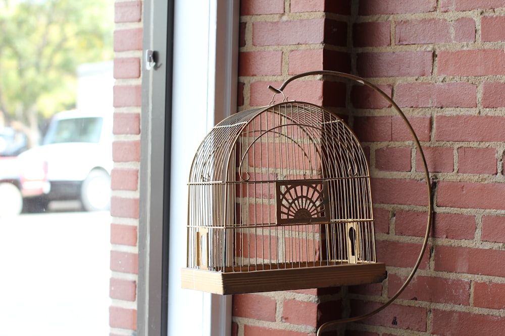 a bird cage hanging on a brick wall