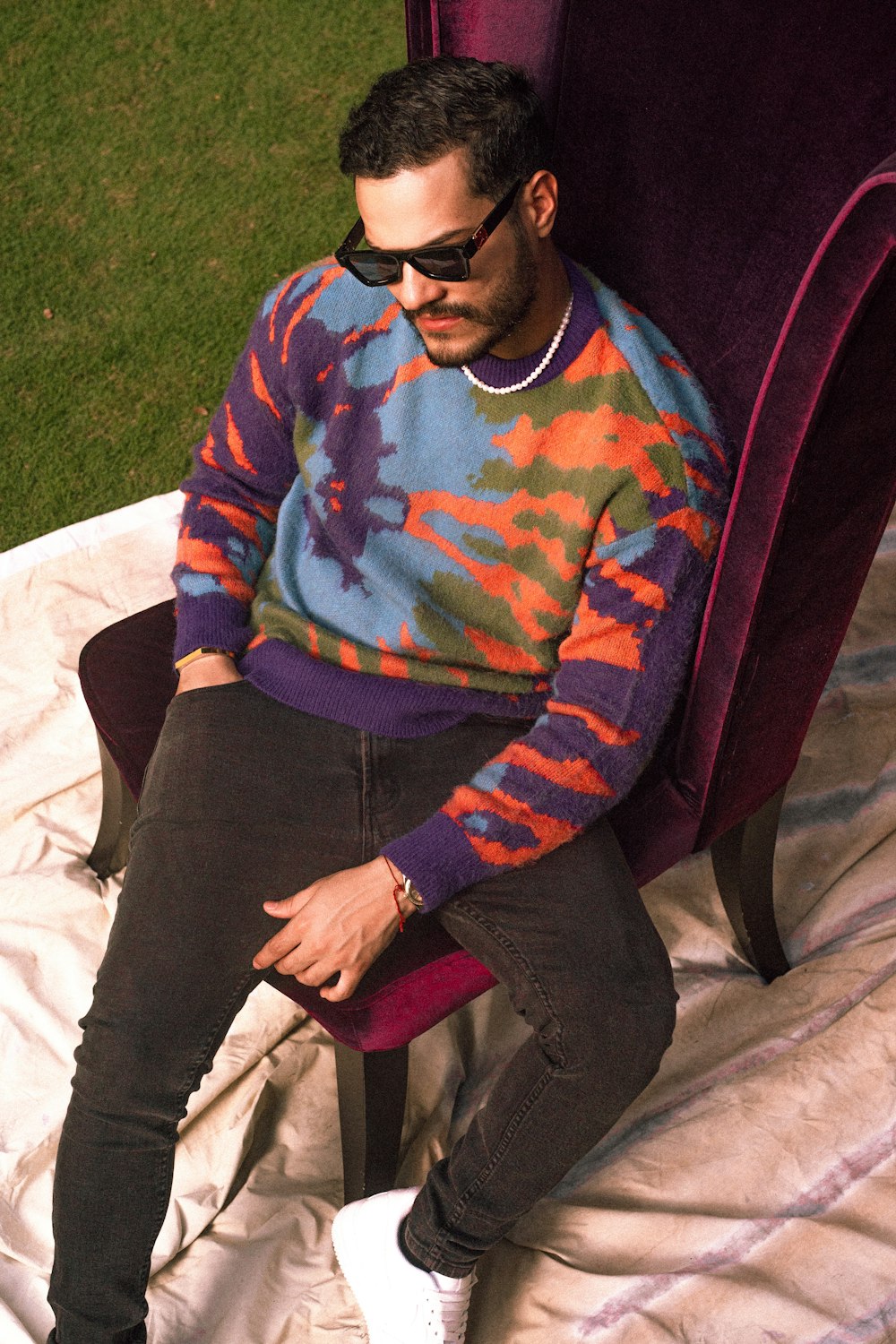 a man sitting in a chair wearing a tie dye sweater