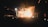 A crowded nightclub with a lively atmosphere. Bright lights and smoke fill the space as people raise their hands in excitement. The stage lights illuminate the area, casting vibrant colors and shadows across the crowd.