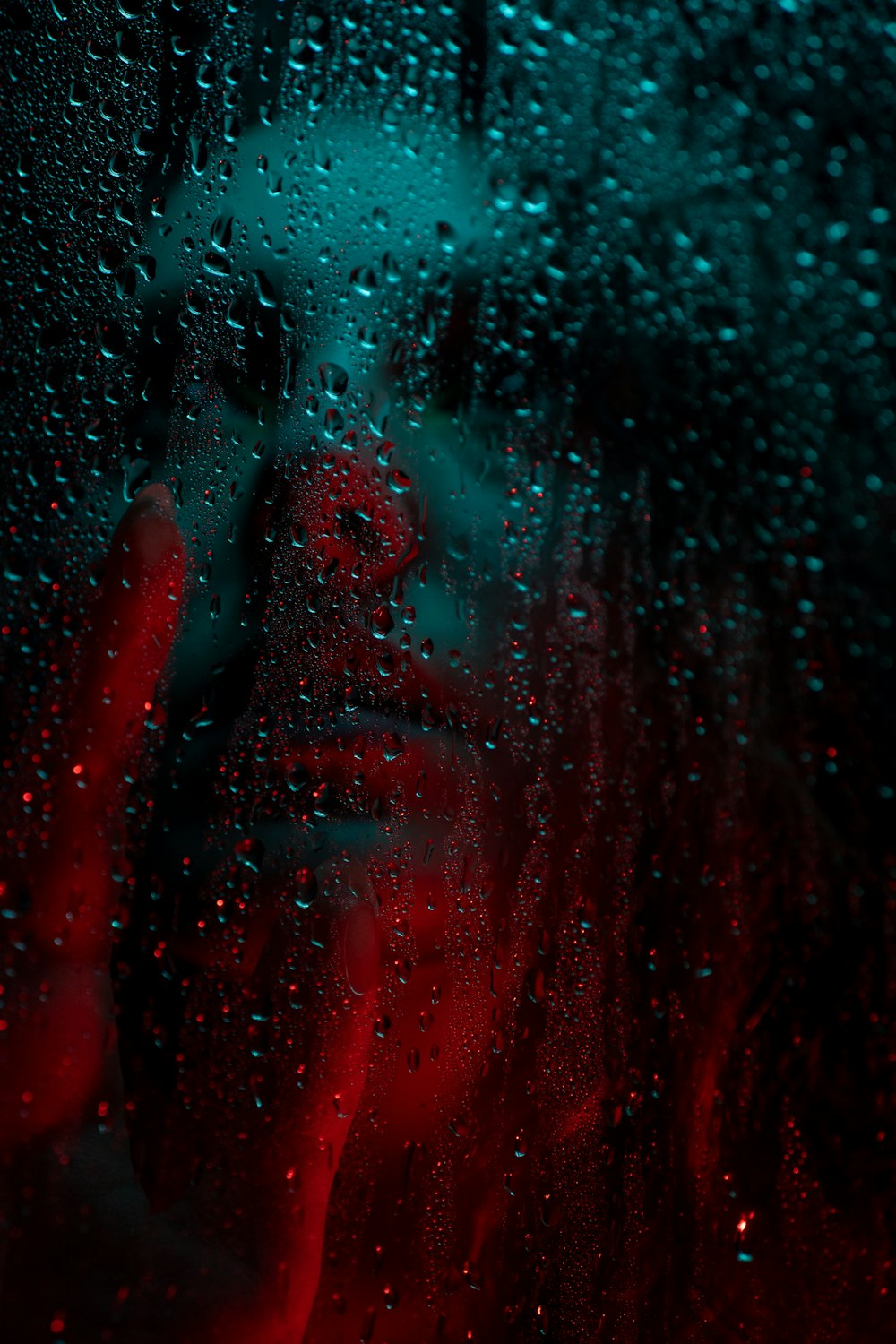 uma mulher é vista através de uma janela coberta de chuva