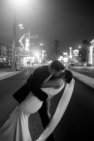 a bride and groom kissing on the street at night